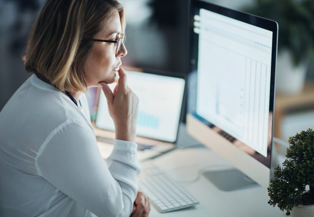 Woman with buttoned up white shirt looking at computer screen with a spreadsheet open.