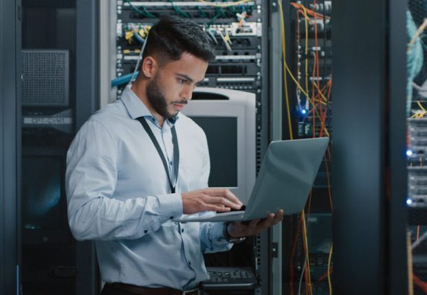 Server expert working on laptop in front of servers.