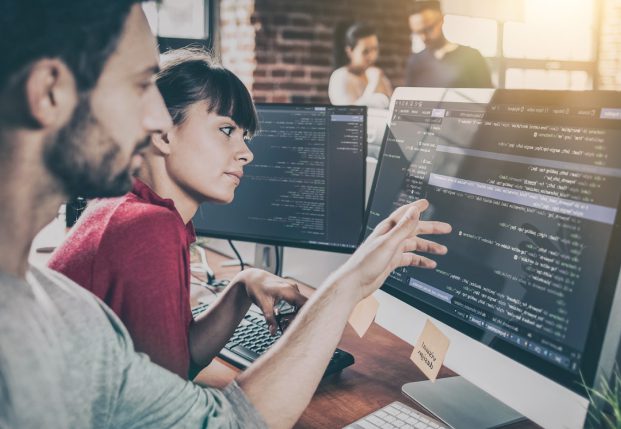 A man and woman collaborate on writing code on a computer screen